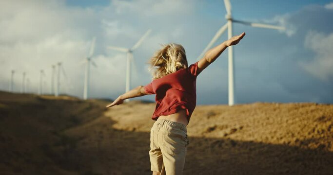 Happy young boy playing in the wind, looking out towards windmills at sunset, clean and sustainable energy concept