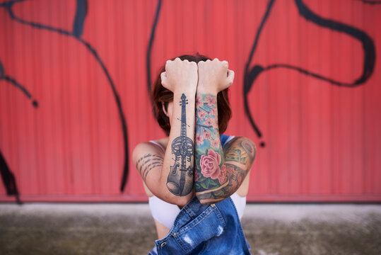 Tattoed brunette blocks her head with hands up.