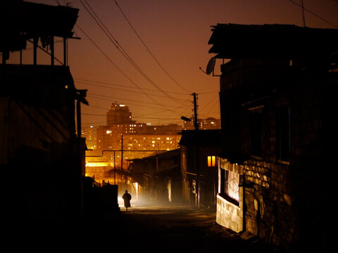 Dark street with solitary figure lit by car headlights.