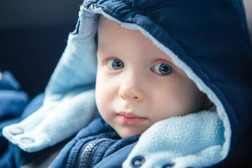 Cute Caucasian baby infant sitting in car seat. Adorable kid in outwear clothes in automobile vehicle carsit fastened with seatbelt. Care, safety and protection of children on road.