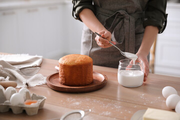 Young woman decorating traditional Easter cake with glaze in kitchen, closeup