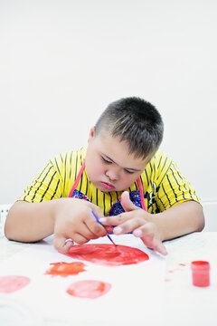 Boy with Down syndrome draw at a table on a white background