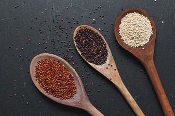 Red, black and white quinoa seeds in different spoons over  black slate stone background. Top view. 