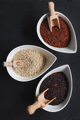 Red, black and white quinoa seeds in bowls on black slate stone background.Top view. Copy space.