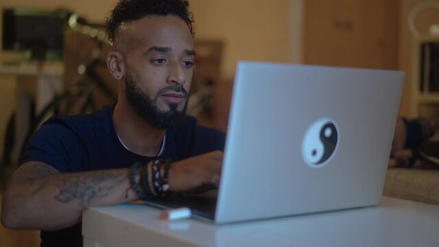 Black man using computer in his home office. African American with dark hair working on the laptop in his home.