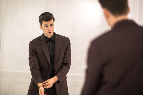 Handsome man wearing a elegant suit fixing and looking at himself in the mirror. - Powered by Adobe