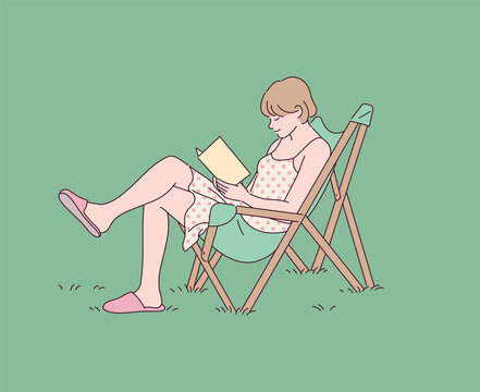A girl is reading a book with a chair on the lawn.