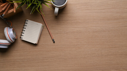 Top view of office desk with coffee cup, headphone, plant, notebook and copy space on wooden...