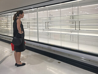 Upset adult woman (age 30-40) looking at Row of empty commercial fridges at grocery store.