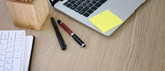Horizontal photo of wooden office desk with laptop and stationery.