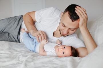 Fototapeta na wymiar Fathers day. Happy proud Caucasian father with newborn baby. Young man dad parent lying on bed hugging kissing child daughter son. Authentic lifestyle candid family moment.