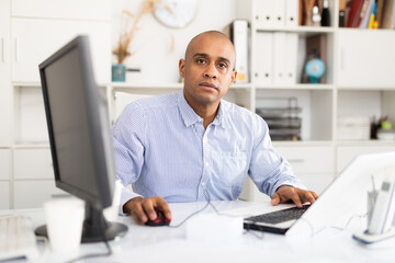 Portrait of handsome hispanic employee looking at camera and sitting at office desk