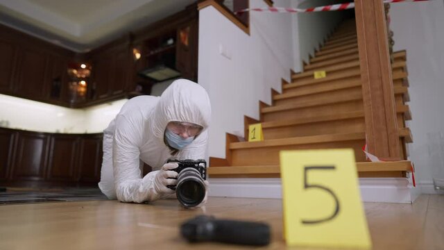 Wide shot of professional concentrated forensic scientist taking photos of clues at crime scene. Portrait of focused Caucasian woman in uniform photographing evidence of robbery or murder indoors.