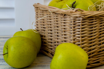 Green apples and basket with apples on wooden background