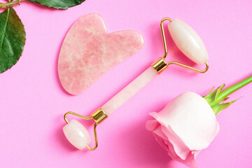 The gua sha and the face roller on pink background, top view