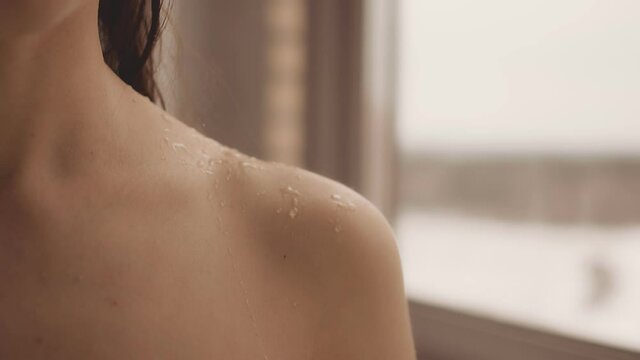 Indoors a naked girl after a shower. Drops of water drip on the girl's shoulder, beautifully spread over the shoulder. Loose dark hair on the back. close-up.