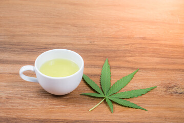 Cup of cannabis tea and cannabis leaf on wooden background