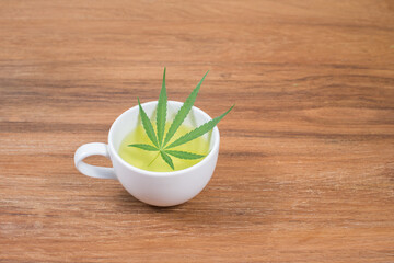 Cup of cannabis tea and cannabis leaf on wooden background
