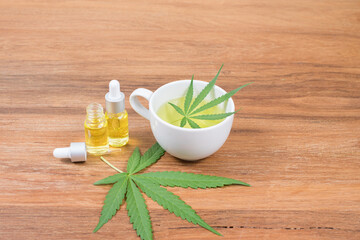 Cannabis tea with cannabis oil extracts in dropper bottle and cannabis leaf on wooden background