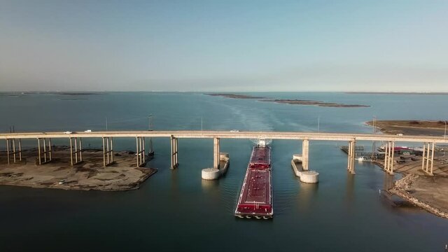 Aerial view of a large red barge moving along the Gulf Intercoastal Waterway and under JFK Memorial Causeway bridge; Corpus Christi Texas