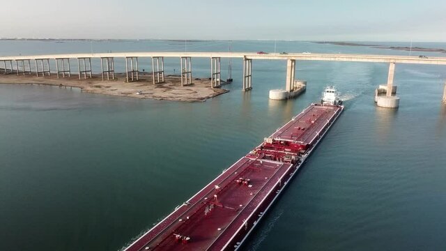 Aerial view of a large red barge moving along the Gulf Intercoastal Waterway and under JFK Memorial Causeway bridge into Laguna Madre; Corpus Christi Texas