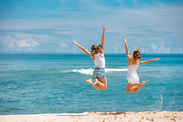 Two young girls jumps against blue sea