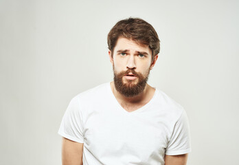 Obraz premium Emotional guy in a white T-shirt on a light background cropped view of a thick beard of a brunette