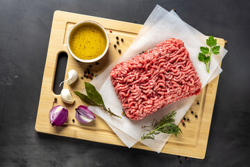 Fresh ground beef on cutting board on dark background with ingredients for cooking top view