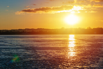 Winter landscape with frozen lake at sunrise or sunset. Lake glistening ice reflect a sun.Forest in the background.