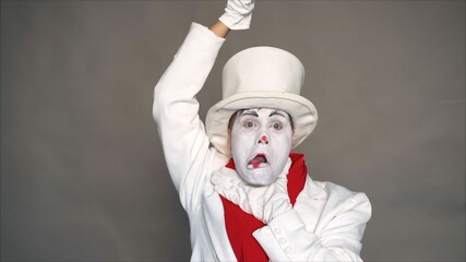 Dangerous mime. Portrait of a joker. Crazy image of a man in a white suit. Mime threatens to camera. The man shows gestures threat.