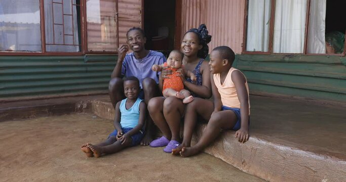 Poor black African family sitting outside their modest tin shack home