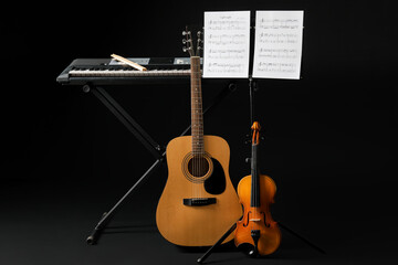 Note stand with music sheets and different musical instruments on dark background