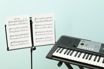 Note stand with music sheets and synthesizer on color background