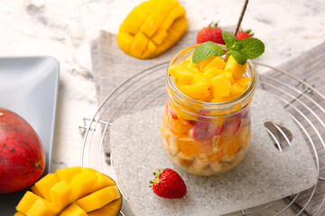 Jar with tropical fruit salad on light background