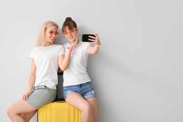 Couple of lesbian tourists taking selfie on light background