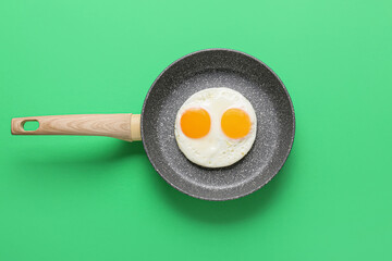 Frying pan with tasty eggs on color background