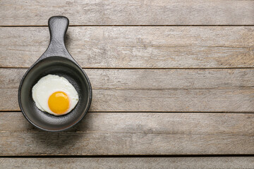 Frying pan with tasty egg on wooden background