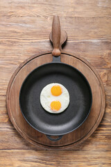 Frying pan with tasty eggs on wooden background
