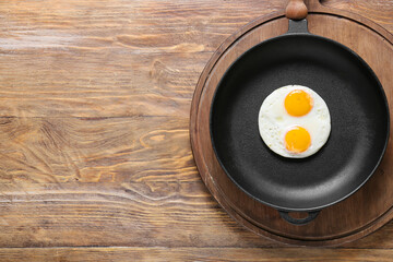 Frying pan with tasty eggs on wooden background