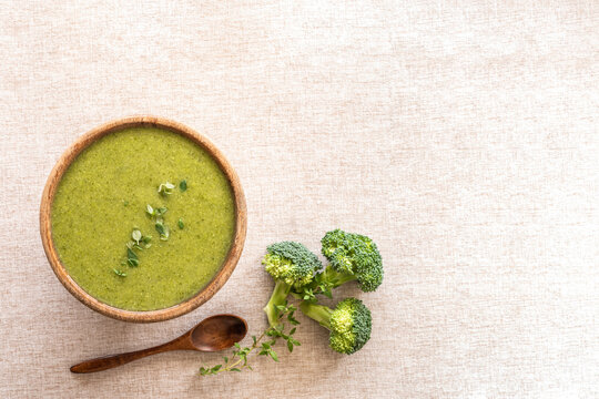 Food background with broccoli soup in wooden bowl over cotton fabric surface.