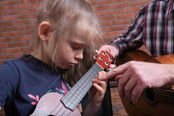 little girl and her father are playing guitar. Learning to play the guitar. Music education and extra-curricular lessons.