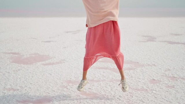 happy positive woman in pink oversize wear funny jogging jumping and running white salty desert background of mineral salt pink lake. woman having fun outdoors, joking and jumping by happiness