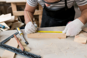 Close up of Man carpenter measuring a wooden board with a ruler with scale in workshop. Joinery work on the production and renovation of wooden furniture. Small Business Concept