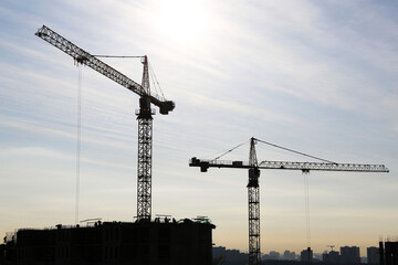 Silhouette of construction crane and workers on unfinished residential building against sunshine. Housing construction, apartment block in city