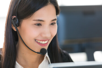 Young and beautiful Asian woman call center officer wearing microphone headset and happy working with a friendly face and positive service mind