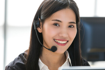 Young and beautiful Asian woman call center officer wearing microphone headset and happy working with a friendly face and positive service mind
