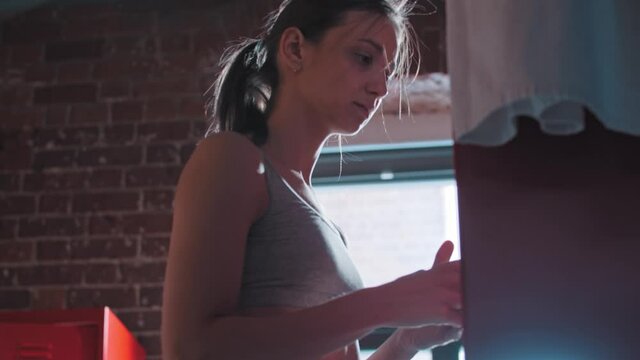 A Young Woman Putting Her Phone In A Locker In Gym Changing Room, Takes A Towel And Walks Away