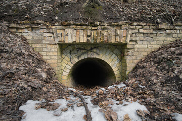Entrance to a dark old abandoned brick tunnel in the woods in sunny day.
