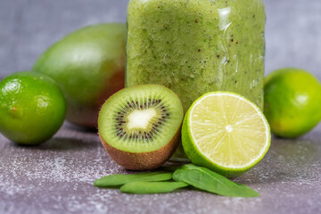 Fototapeta na wymiar Close-up of fresh kiwi and lime fruit halves against a smoothie mug on a gray