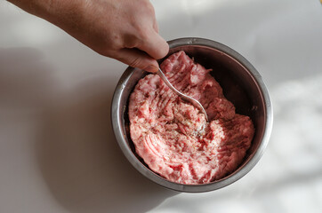 Hand stirring minced meat with a fork in a bowl on a light table